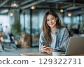 Young asian woman using mobile phone and laptop in a modern co-working space smiling charmingly 129322731
