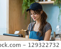 Young female barista working at a modern coffee shop smiling while taking orders with POS system 129322732