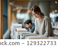 Young female student researching books in a university library during the day with dedication and 129322733
