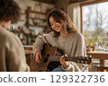 Young woman enjoys playing acoustic guitar while sharing music with a friend indoors 129322736