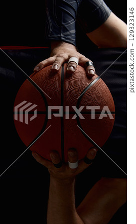 Two hands gripping basketball with taped fingers in dramatic light Two hands gripping basketball with taped fingers in dramatic light 129323146