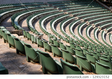 Large, open-air stone amphitheater is filled with numerous rows of green plastic seats arranged in a semi-circular pattern 129323152