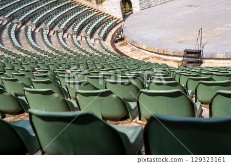 Amphitheater with concentric rows of tiered seating curving around a central stage area under an open sky Amphitheater with concentric rows of tiered seating curving around a central stage area under an open sky 129323161