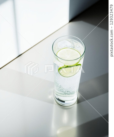 Glass of water with lime slices and ice, refreshing drink on a bright surface. 129323479