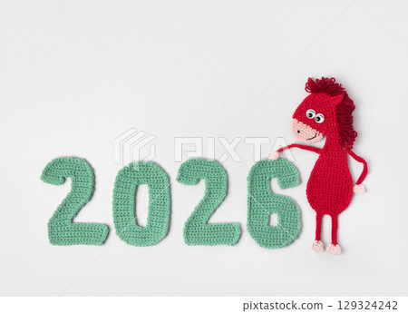 Crocheted toy fiery red horse and green numbers. The symbol of the year 2026 on a gray background. 129324242