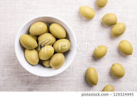 Green olives with pit, in a white bowl on linen. Whole, large table olives, harvested before fully ripe, with a more tangy and briny flavor, preserved in wine vinegar and salt, to remove bitterness. 129324945