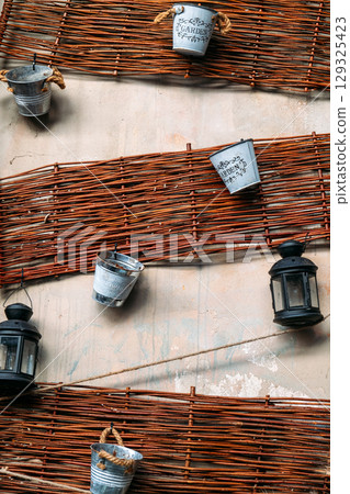 Metal buckets labeled for gardening hang alongside black lanterns on woven wooden slats fixed to a wall. Handmade planters, eco DIY, upcycled materials, creative reuse 129325423