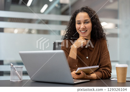 Confident woman with a notepad and laptop enjoying her work in a stylish office. The setting is informal yet professional, suggesting productivity, creativity, and modern workplace design. Confident woman with a notepad and laptop enjoying her work in a stylish office. The setting is informal yet professional, suggesting productivity, creativity, and modern workplace design. 129326104