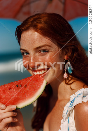 A woman is holding a slice of watermelon and smiling 129326244