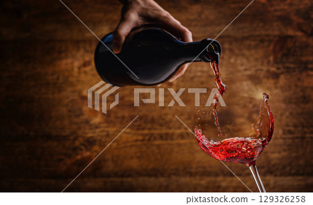 Red wine splashing into a glass with a rustic wooden background Red wine splashing into a glass with a rustic wooden background 129326258
