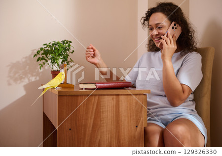 Woman Using Phone Near Parakeet on Desk in Home Office Setting Woman Using Phone Near Parakeet on Desk in Home Office Setting 129326330