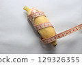 A short yellow banana wrapped with a measuring tape, placed on a clean white background. This image highlights both the length and circumference of the fruit. 129326355