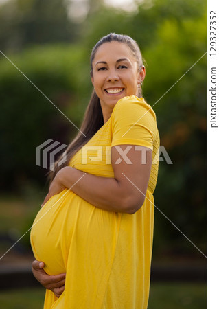 Smiling Pregnant Woman Outdoors in a Yellow Dress on a Sunny Day 129327352