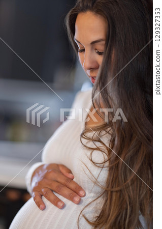 Pregnant woman gently holding belly in a serene indoor setting 129327353