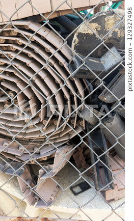 Piled plastic materials and equipment behind a chain-link fence, showcasing a variety of shapes and textures in an industrial storage area with a sense of organization and clutter Piled plastic materials and equipment behind a chain-link fence, showcasing a variety of shapes and textures in an industrial storage area with a sense of organization and clutter 129327498