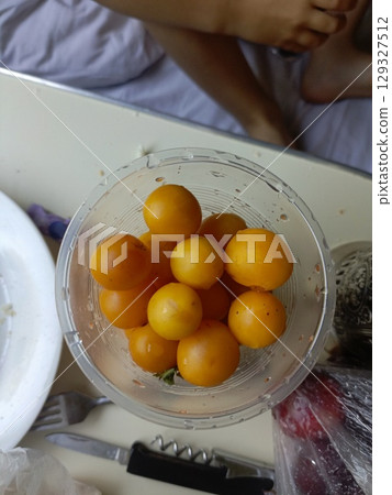 Yellow cherry tomatoes in a clear bowl in a high-angle, casual style representing fresh ingredients and healthy snacking 129327512
