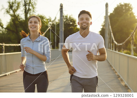 Sporty people man and woman running together along a bridge having sport workout outdoors. 129328001