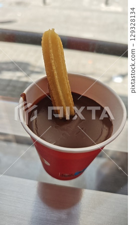 Traditional Spanish churro dipped into a thick cup of hot chocolate served in a red paper cup Traditional Spanish churro dipped into a thick cup of hot chocolate served in a red paper cup 129328134
