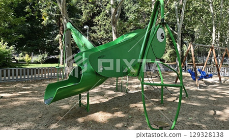 Modern childrens playground with a green insect-shaped slide structure in a shaded park area Modern childrens playground with a green insect-shaped slide structure in a shaded park area 129328138