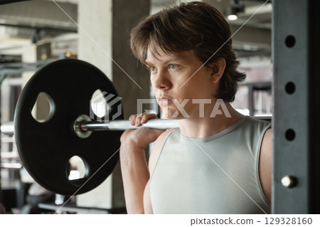 Confident young man exercising with barbell at fitness center. Cross training. Male athlete lifting weights. 129328160