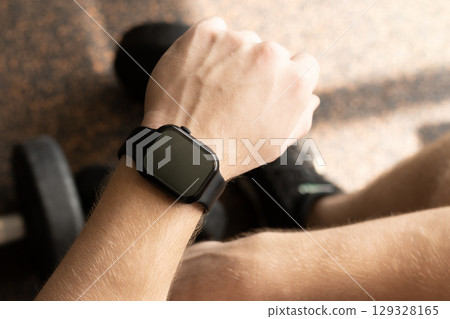 Hand gym with smartwatch on wrist, set against background with gym equipment. Check fitness progress in apps. Mock up. 129328165