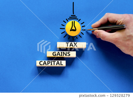 Capital gains tax symbol. Concept words Capital gains tax on beautiful wooden block. Businessman's hand. Beautiful blue background. Business and capital gains tax concept. Copy space. 129328279