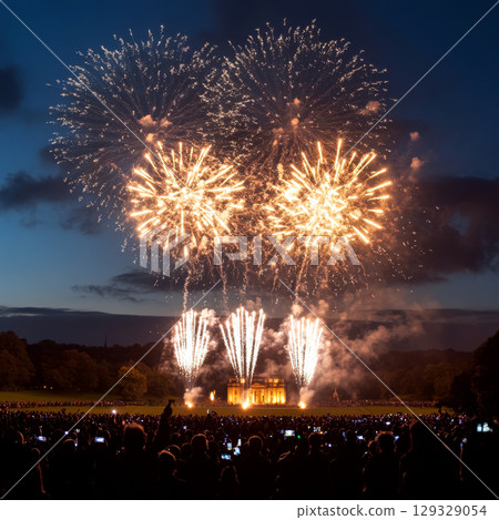 Fireworks burst over an illuminated building at night, watched by a large crowd. Concept of celebration and festivity. For event photography. 129329054