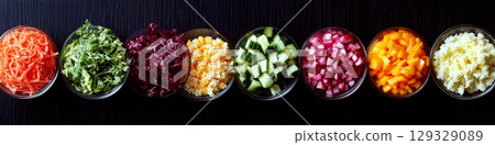 A row of bowls containing colorful, chopped vegetables is placed on a dark surface. Concept of diversity in fresh ingredients. For healthy eating inspiration. 129329089