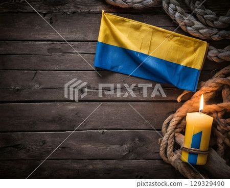 Folded Ukrainian Flag with Burning Candle on Wooden Background 129329490