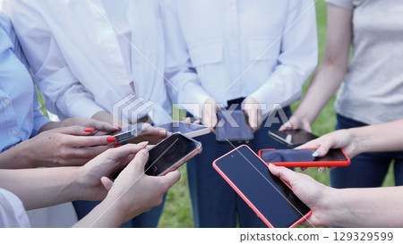 A diverse group of individuals is gathering outdoors in a relaxed manner, all actively engaged with their smartphones A diverse group of individuals is gathering outdoors in a relaxed manner, all actively engaged with their smartphones 129329599