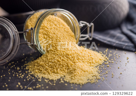 Raw couscous in jar on black table. 129329622
