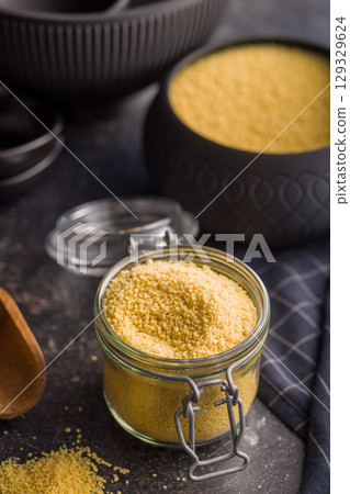 Raw couscous in jar on black table. 129329624