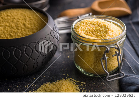 Raw couscous in jar on black table. 129329625
