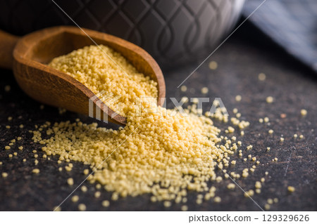 Raw couscous in scoop on black table. 129329626