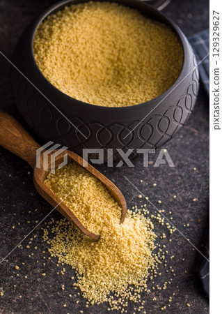 Raw couscous in scoop on black table. Raw couscous in scoop on black table. 129329627