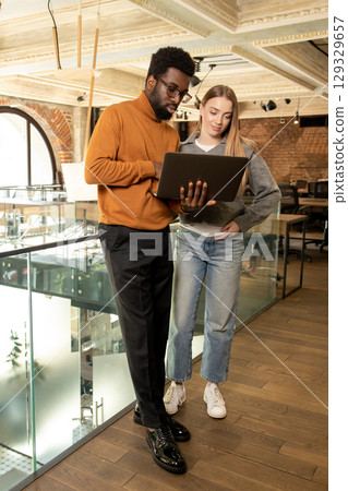 Two diverse coworkers standing and talking working on strategy in contemporary open office 129329657