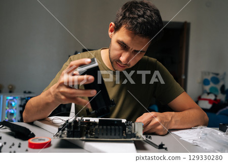 Portrait of focused computer technician installing CPU cooler onto motherboard, performing maintenance or upgrade in specialized workshop environment. Concept of desktop PC maintenance and service. Portrait of focused computer technician installing CPU cooler onto motherboard, performing maintenance or upgrade in specialized workshop environment. Concept of desktop PC maintenance and service. 129330280