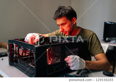 Computer technician wearing protective white gloves carefully installing internal hardware components inside open desktop computer case, glowing with red illumination during technical maintenance. 129330283