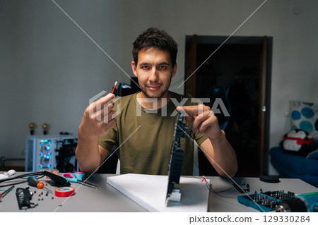 Portrait of computer service technician repairing computer part while holding cotton swab and looking at camera, sitting at desk in workshop environment. Concept of service, repair, cleaning computer. 129330284