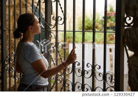 Woman Contemplating Through Ornate Iron Fence on Sunny Day 129330427