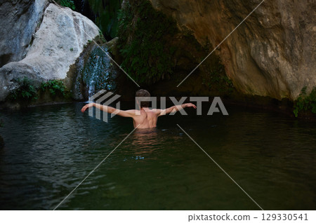 Man Bathing in a Serene Rock Pool Surrounded by Natural Greenery Man Bathing in a Serene Rock Pool Surrounded by Natural Greenery 129330541