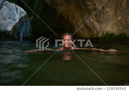 Relaxed Man Swimming in a Serene Natural Spring Surrounded by Rocks 129330543