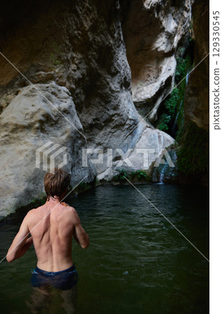 Man Exploring a Scenic Natural Canyon Pool with a Waterfall Man Exploring a Scenic Natural Canyon Pool with a Waterfall 129330545