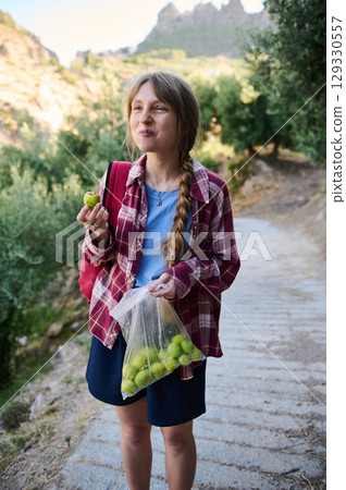 A Woman Enjoying Fresh Green Fruits While Walking in a Hilly Rural Area, Exuding a Happy and Relaxed Mood 129330557