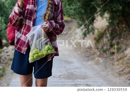 Young Woman Holding a Bag of Freshly Picked Green Figs on a Rural Pathway 129330559