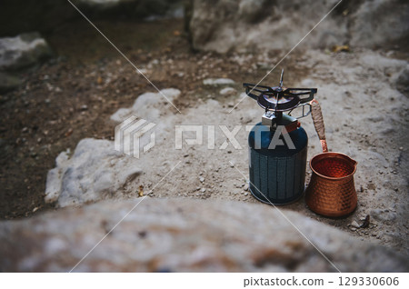 Portable Camping Gas Stove and Copper Pot on Outdoor Rocky Ground 129330606