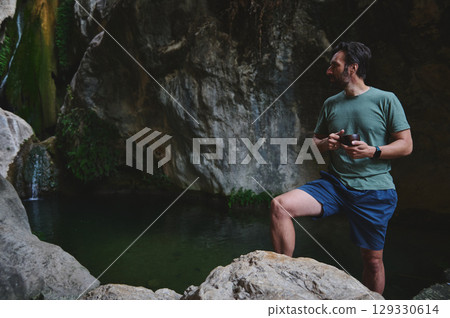 Man Relaxing Near a Scenic Rocky Waterfall in a Tranquil Forest Man Relaxing Near a Scenic Rocky Waterfall in a Tranquil Forest 129330614