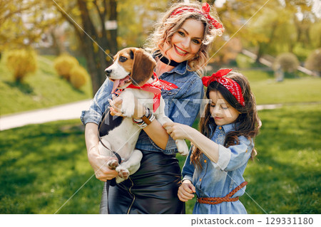 Beautiful mother with daughter. Family in a spring park. Woman in a blue shirt. Family with a cute dog 129331180