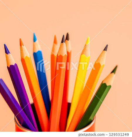 Multicolored pencils arranged in a red metal cup on a soft peach background. Minimalist and vibrant concept for education, creativity, design, and back to school. Bright tones with copy space. 129331249