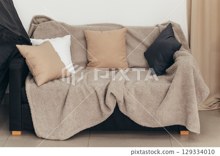 A cozy sofa with colored pillows and a blanket against a light wall. Living room interior design idea 129334010